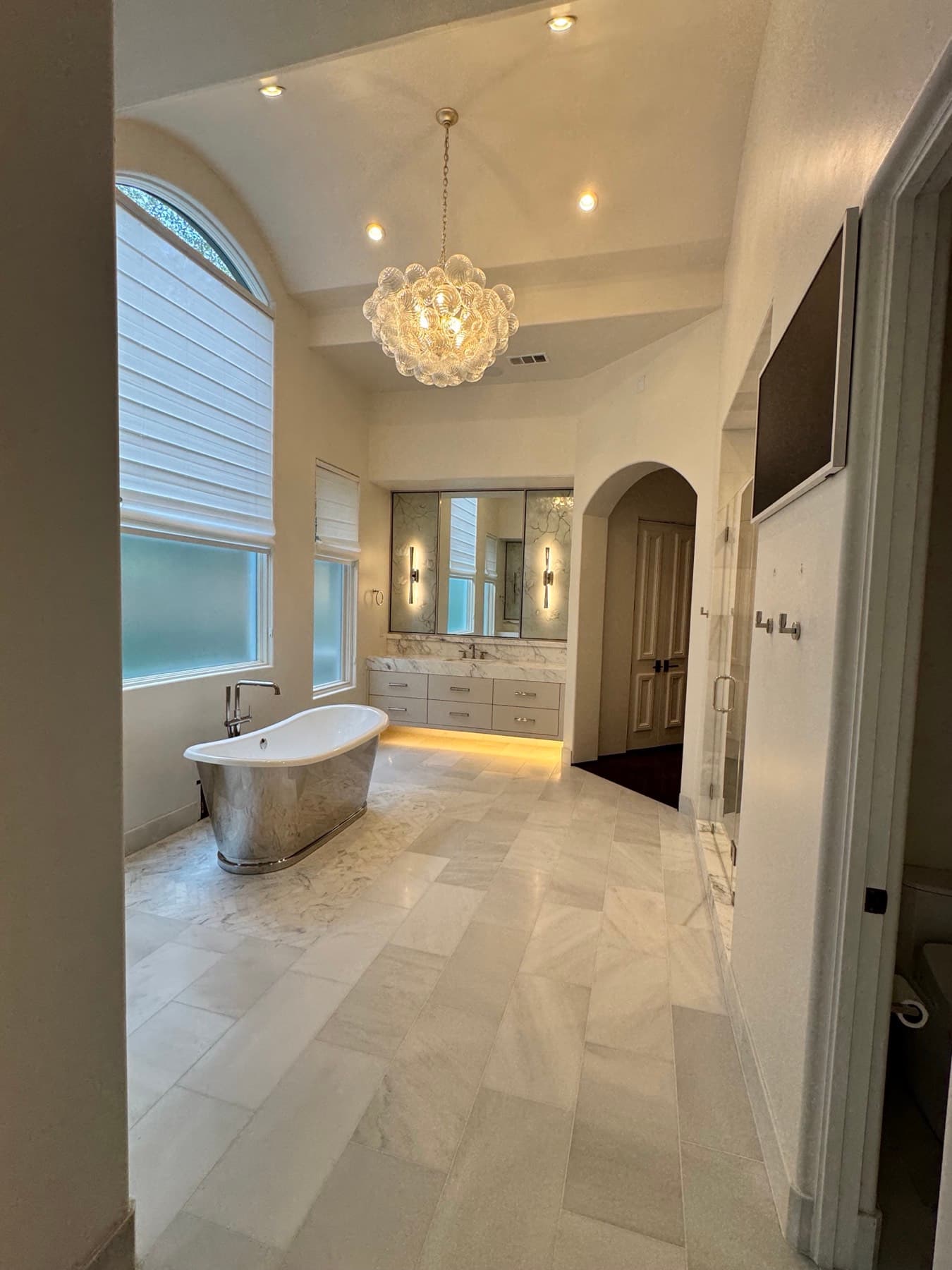 Luxury master bath with a glass chandelier, backlit mirror sconces, and under-vanity LED lighting