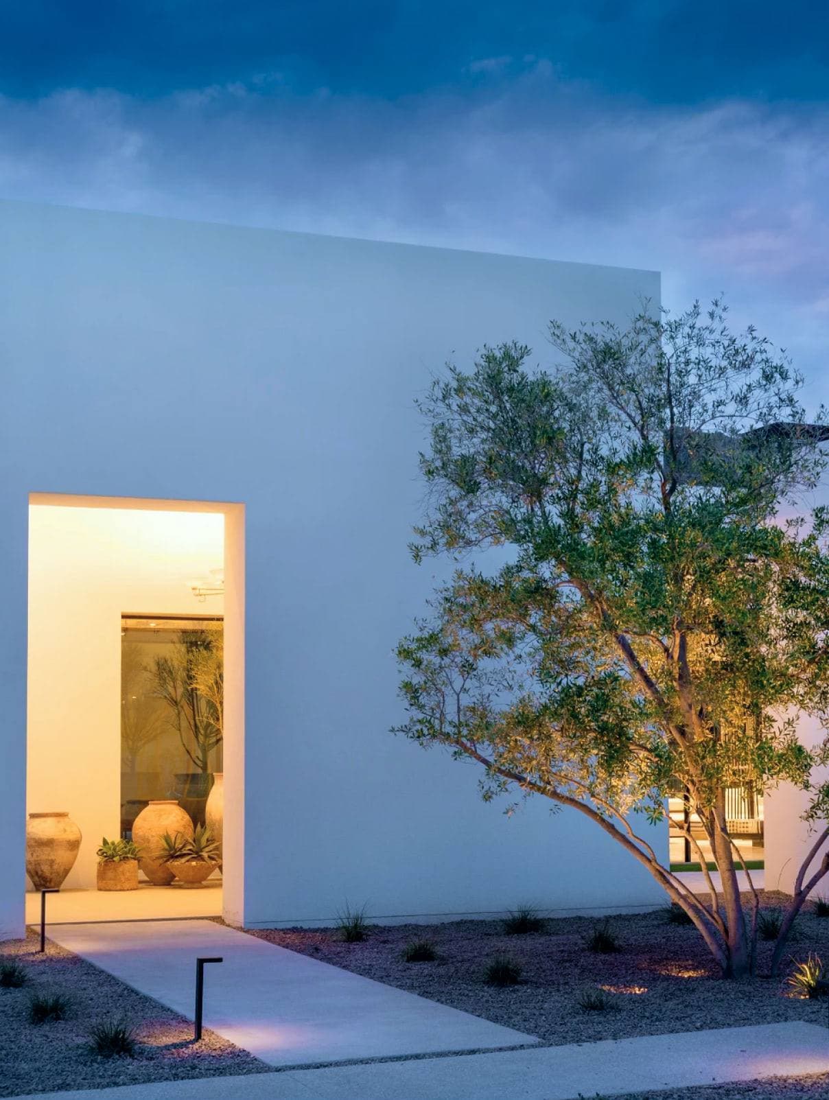 Modern home at dusk with landscape lighting, representing one-touch Crestron comfort and lighting control