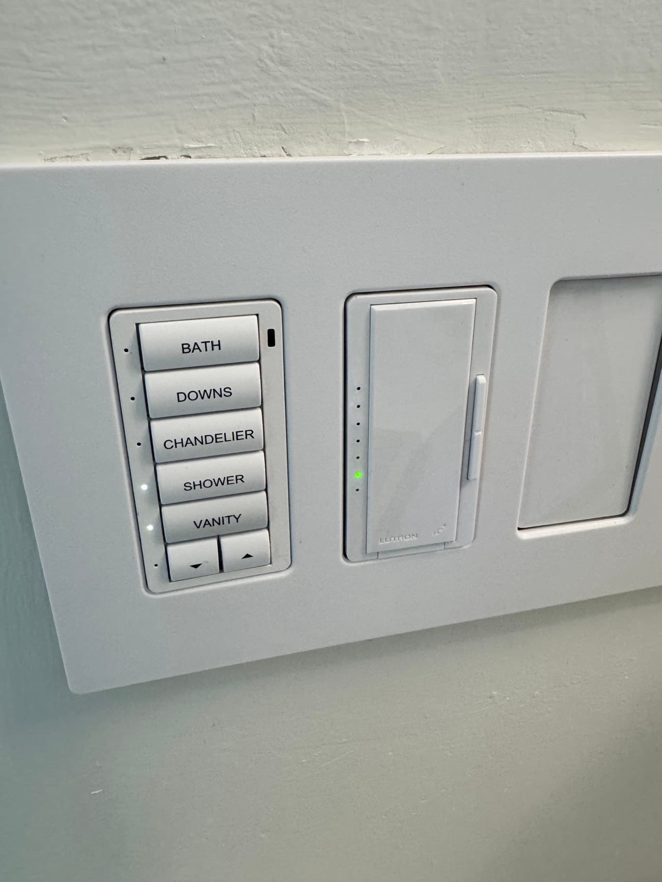Engraved wall keypad with bath, chandelier, shower, and vanity lighting scenes beside a dimmer