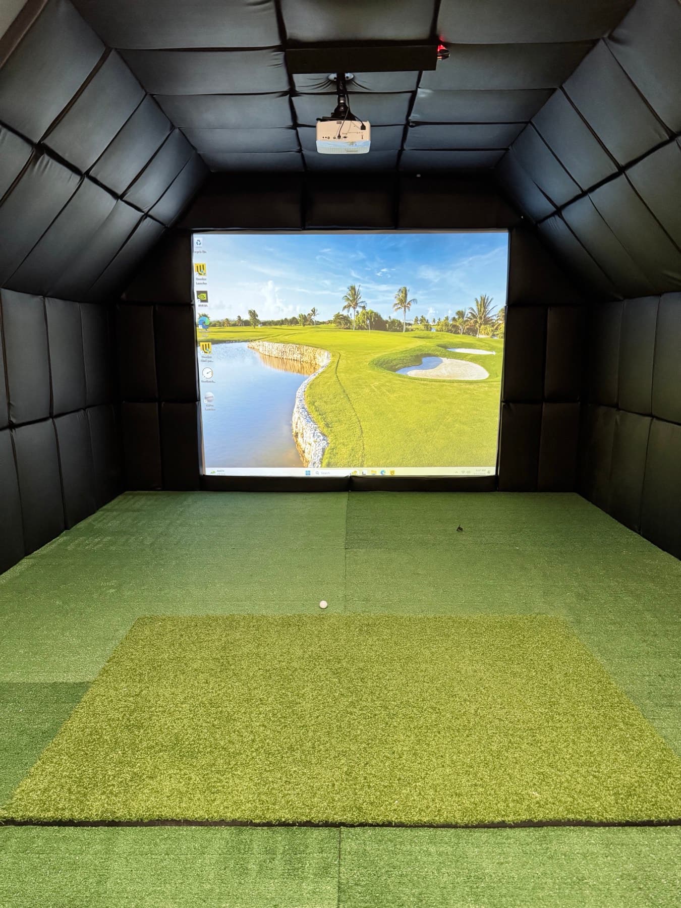 Enclosed indoor golf simulator bay with projection impact screen and turf